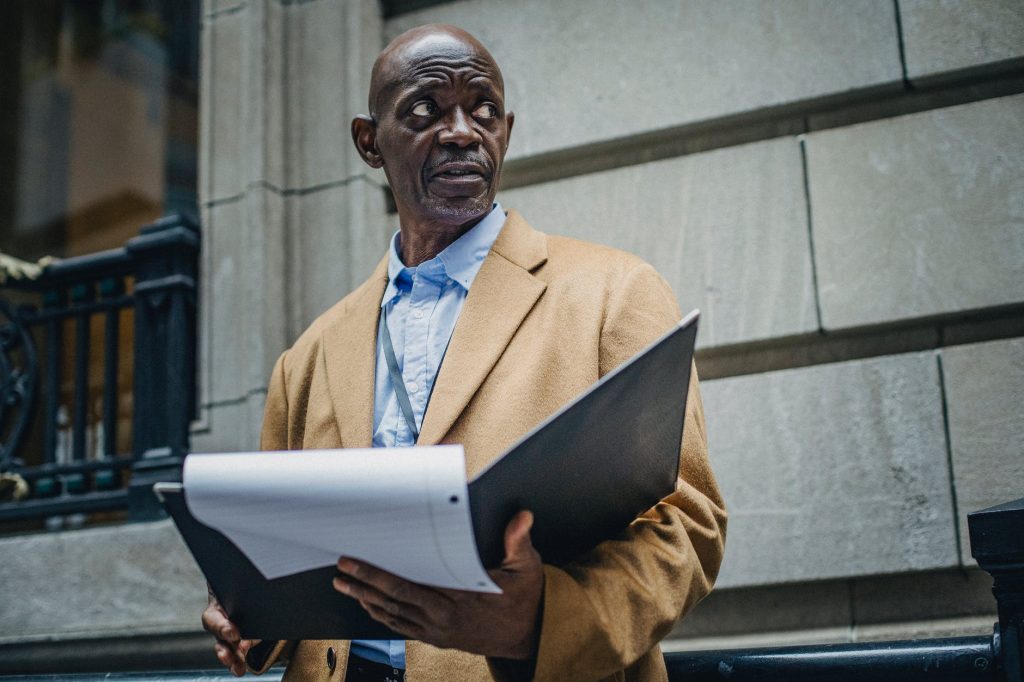 thoughtful black entrepreneur with folder standing on street